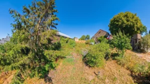 Jardin arboré avec des maisons en pierre en arrière-plan sous un ciel bleu ensoleillé